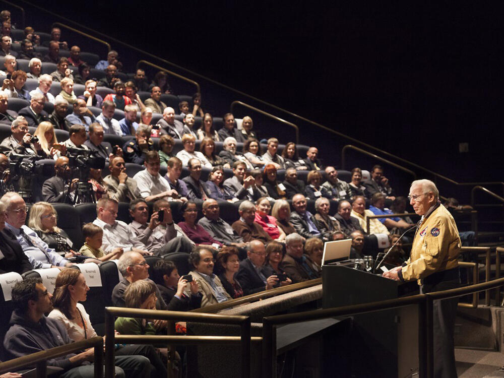 Jim Lovell, an elderly man in a NASA flight jaket, speaks to a young boy in the audience.
