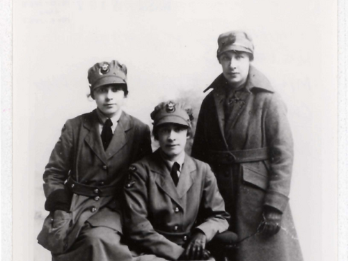 Three women pose for a photo. One sits in front while the two others flank her on either side. They are all wearing military uniforms.